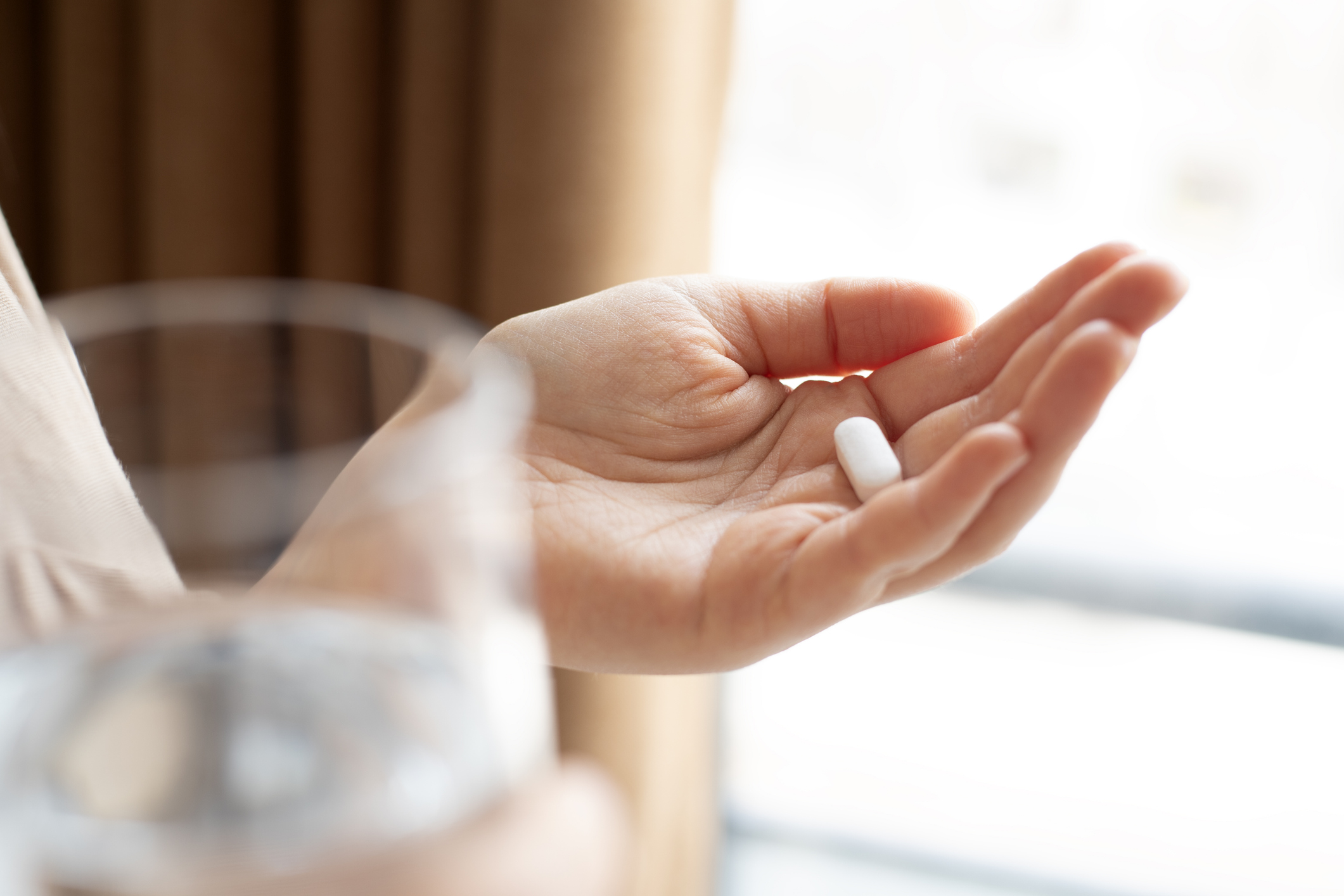 Woman hand holding antibiotic pill and glass of water