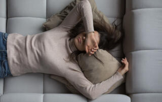 Woman lying on back with hand over her face in pain