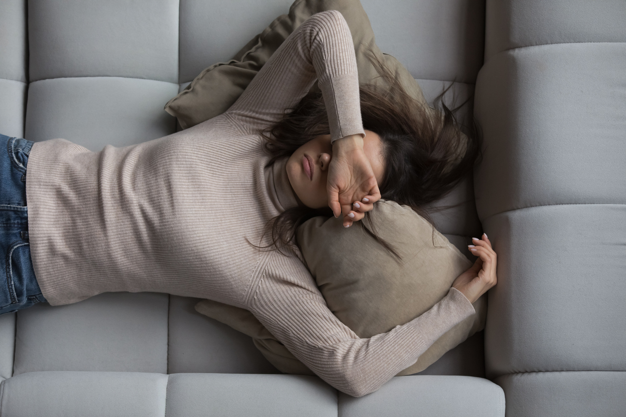 Woman lying on back with hand over her face in pain